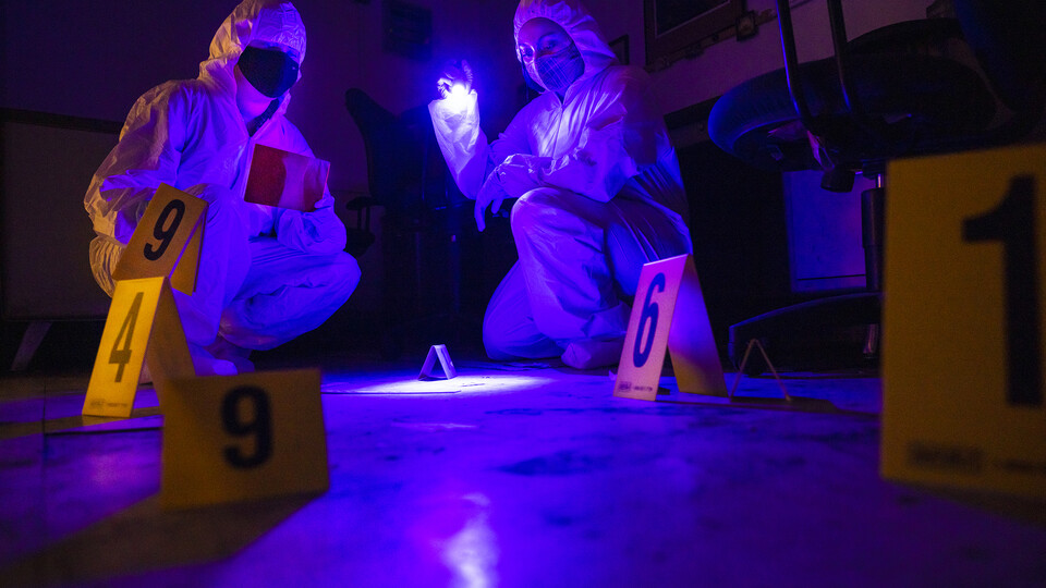Forensic Science students in sterile suits collect evidence from a crime scene