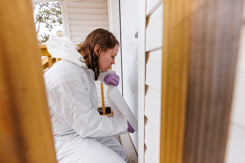 A student works at the front door of a house investigating a crime scene.