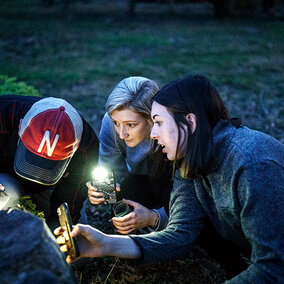 Three forensic scientists are out in a field using their phone flashlights to investigate